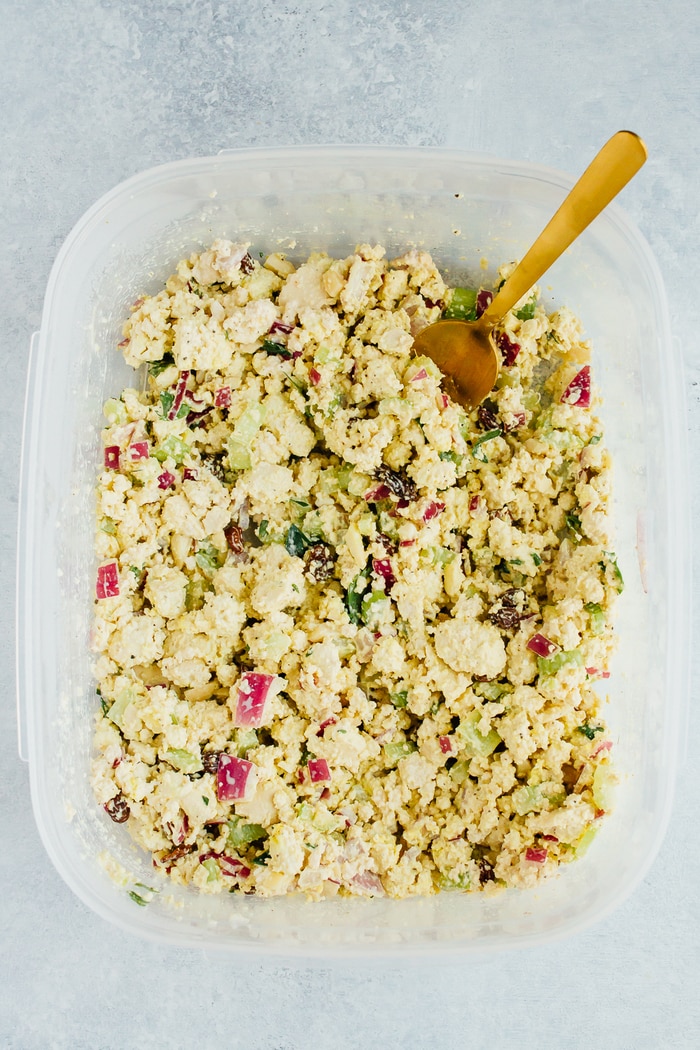 Overhead photo of clear tupperware of Vegan Chicken Salad made with tofu, celery, almonds and raisins on white countertop.