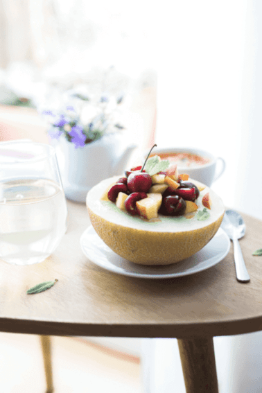 A melon breakfast bowl filled with fresh fruit on a table alongside a glass of water.
