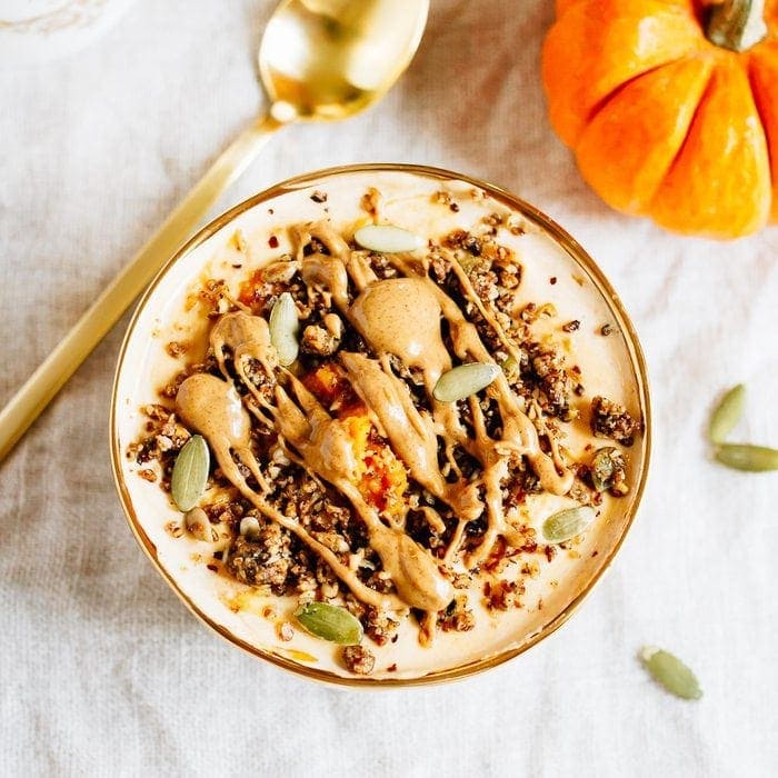 This pumpkin pie yogurt bowl is the perfect fall breakfast. Loaded with protein-packed yogurt, pumpkin puree, pumpkin pie spice and all your favorite toppings! Bowl filled with yogurt and pumpkin and topped with seeds, granola and almond butter. Spoon and pumpkin off to the side.