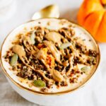 Pumpkin pie yogurt bowl topped with pumpkin seeds, granola and a drizzle of almond butter.