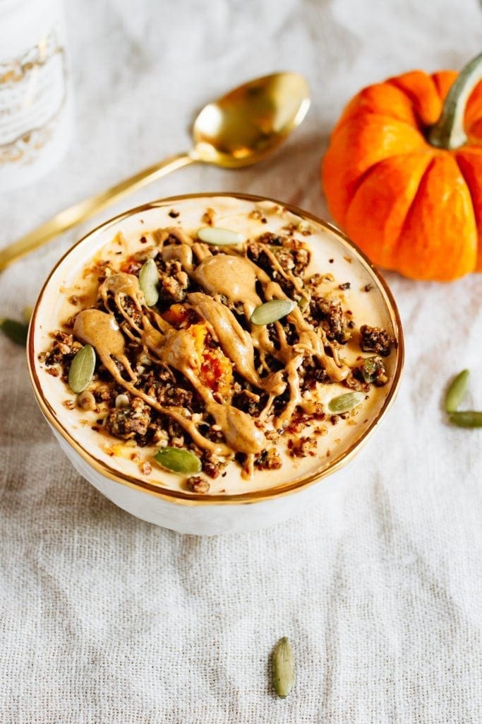 This pumpkin pie yogurt bowl is the perfect fall breakfast. Loaded with protein-packed yogurt, pumpkin puree, pumpkin pie spice and all your favorite toppings! Bowl filled with yogurt and pumpkin and topped with seeds, granola and almond butter. Spoon and pumpkin off to the side.