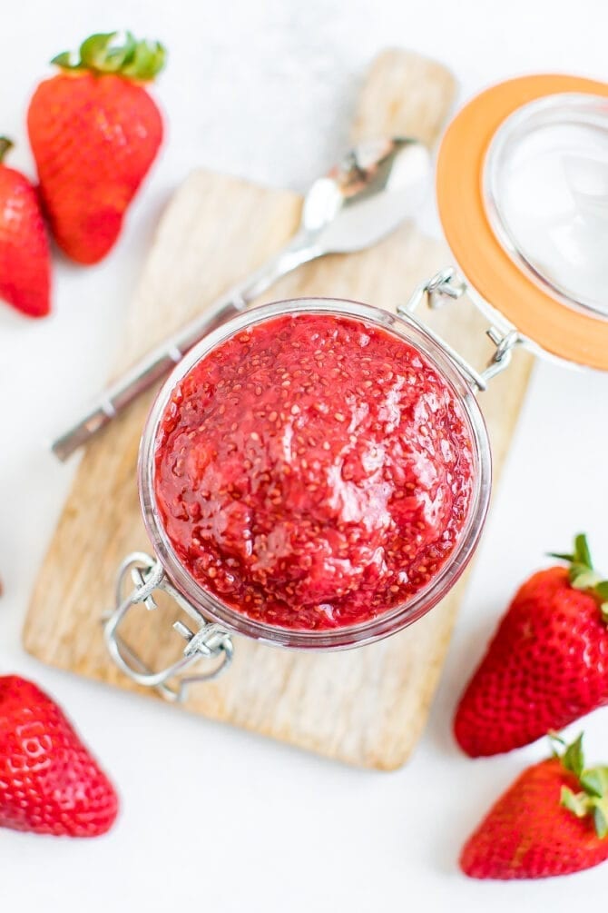 Close-up overhead photo of strawberry chia jam in a glass jar with fresh strawberries around the outside.
