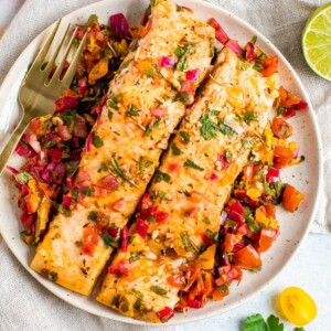 Baked salmon served on a white plate with a golden fork.