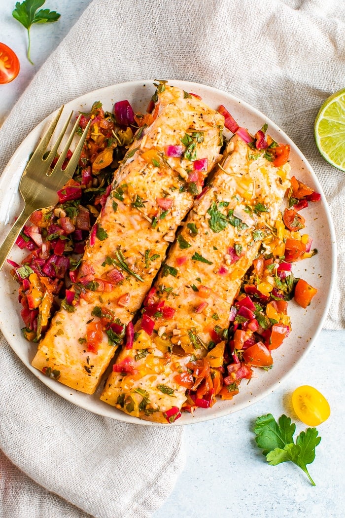 Baked salmon served on a white plate with a golden fork.
