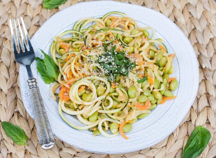zucchini noodle pad Thai, with edamame, topped with chopped fresh basil leaves, on a white plate. A silver fork is sitting on the plate.