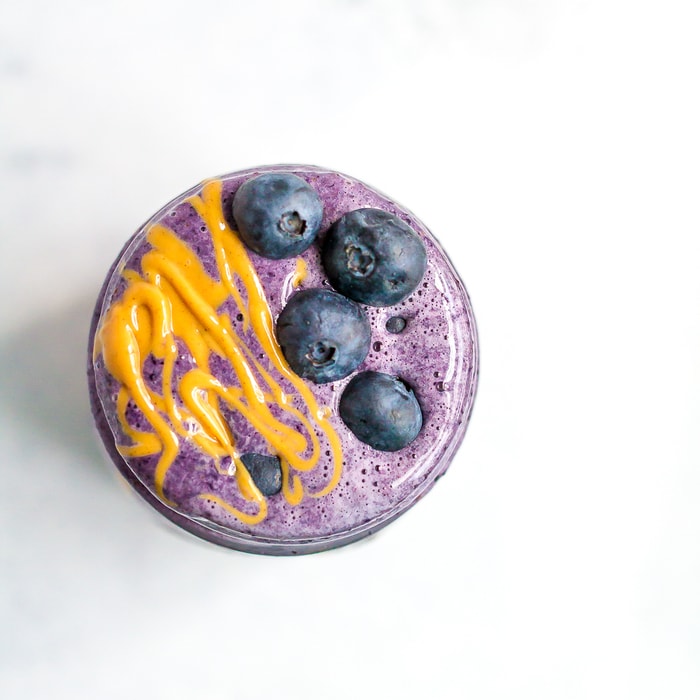 PEANUT BUTTER AND JELLY SMOOTHIE A blueberry smoothie with fresh blueberries and a drizzle of peanut butter in a mason jar.