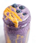 A serving of a blueberry smoothie with a drizzle of peanut butter in a glass mason jar.