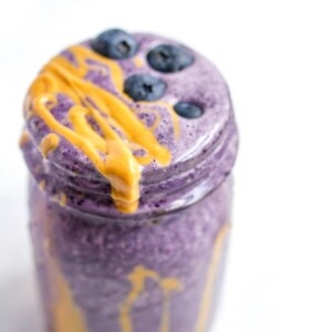 A serving of a blueberry smoothie with a drizzle of peanut butter in a glass mason jar.