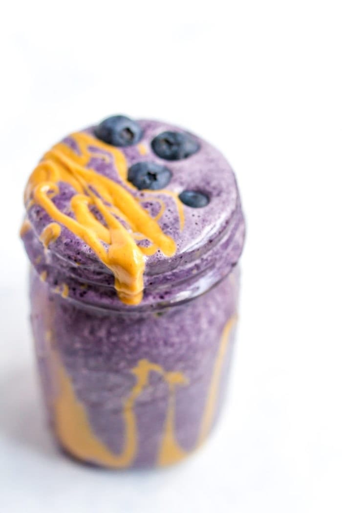 A serving of a blueberry smoothie with a drizzle of peanut butter in a glass mason jar.