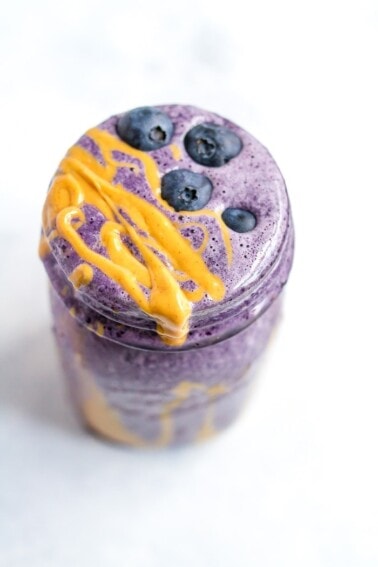 A blueberry smoothie in a glass mason jar topped with fresh blueberries and peanut butter.