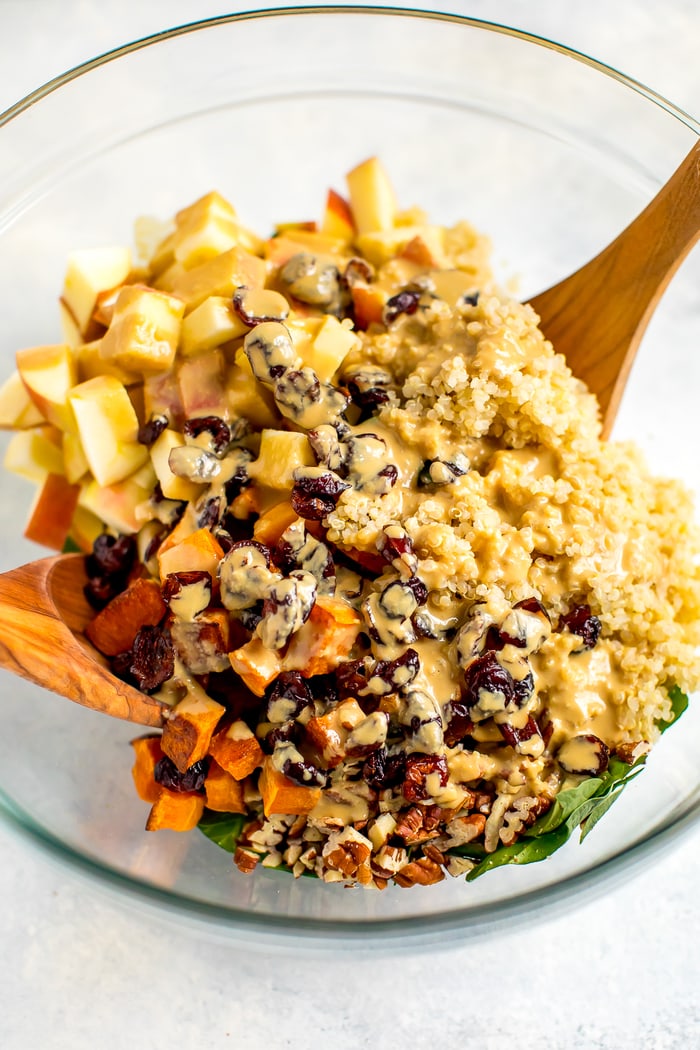 Ingredients for the fall harvest salad in a glass bowl being tossed with a vinegar tahini dressing.