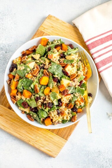 A serving of a fall harvest salad with apple, pecans, spinach, and quinoa in a bowl with a metal fork.