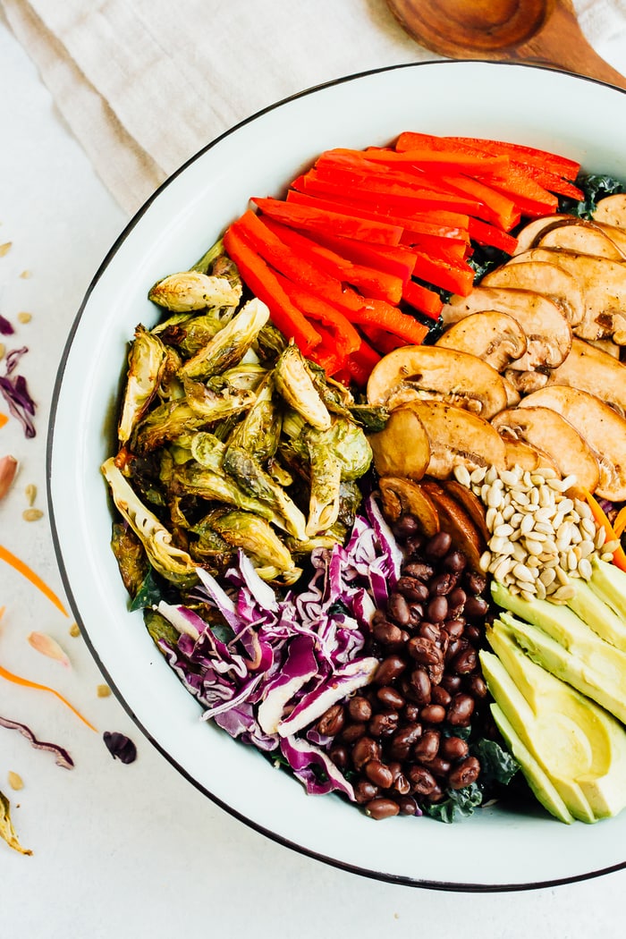 Pin this image for a nourishing detox kale salad! Close up overhead photo of large salad bowl with ingredients spread around bowl.