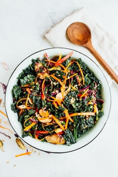 A large bowl of kale salad with sliced avocado on top. Wooden spoon is on the side of the bowl.