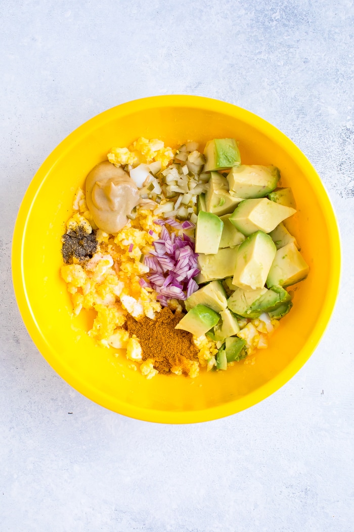 A yellow bowl with all the ingredients to make curried avocado egg salad.