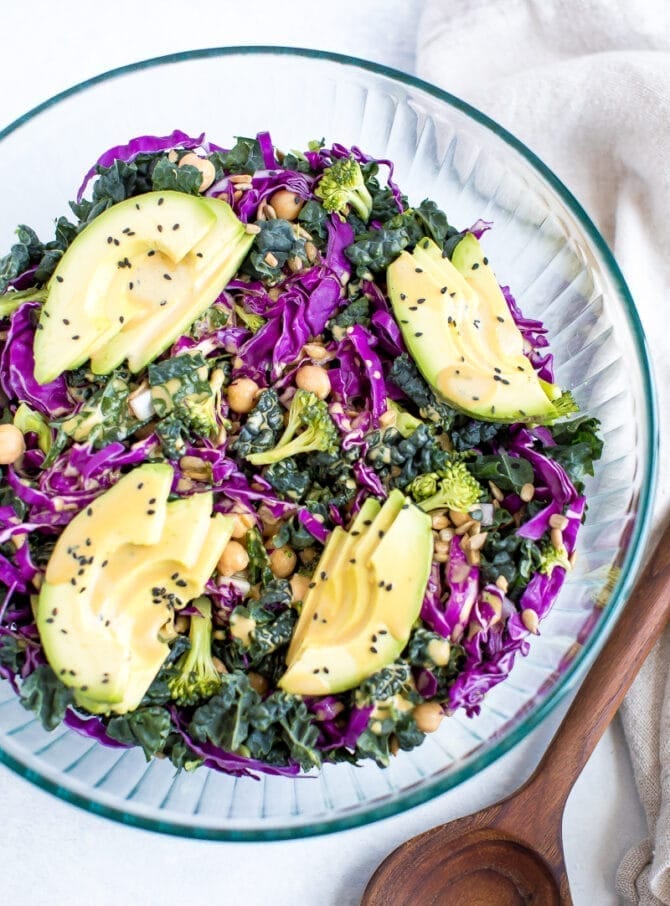 A serving of salad with kale, cabbage, avocado, broccoli, chickpeas, and a nutritional yeast goddess dressing in a bowl.