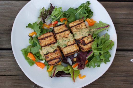 Grilled Lemon Basil Tofu Lemon basil tofu served over a bed of mixed greens on a white plate drizzled with a sauce.