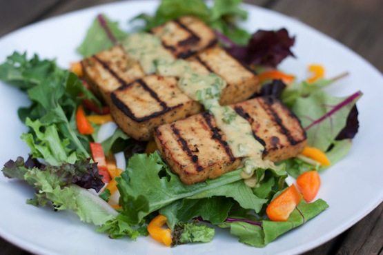This lemon basil tofu is marinated in a zesty fresh basil sauce and grilled to perfection. It's easy and absolutely delicious! A plate with basil lemon tofu on a bed of mixed greens.