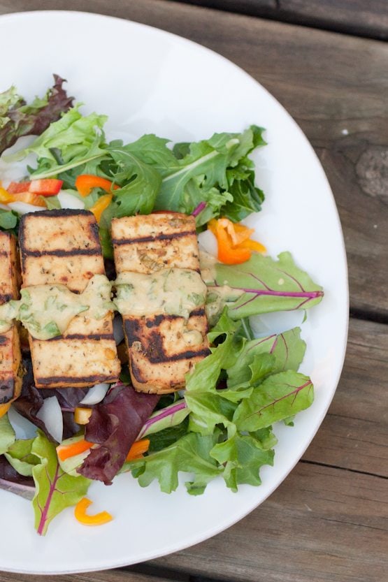 This lemon basil tofu is marinated in a zesty fresh basil sauce and grilled to perfection. It's easy and absolutely delicious! Lemon basil tofu served over a bed of mixed greens on a white plate.
