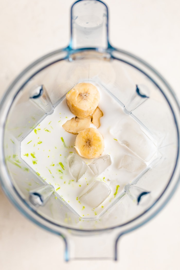 Vitamix blender overhead photo with coconut milk, banana chunks, ice and lime zest.