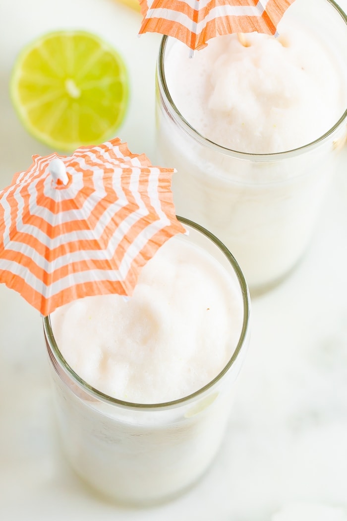 Two skinny coconut daiquiris in tall glasses served with little umbrellas.