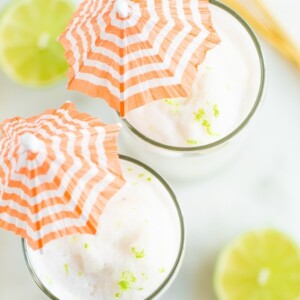 Two skinny coconut daiquiris in tall glasses with orange and white striped cocktail umbrellas.