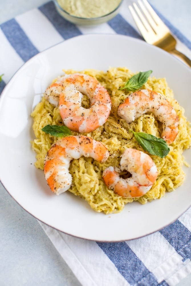 Pesto spaghetti squash in a bowl served with seasoned shrimp and fresh basil.