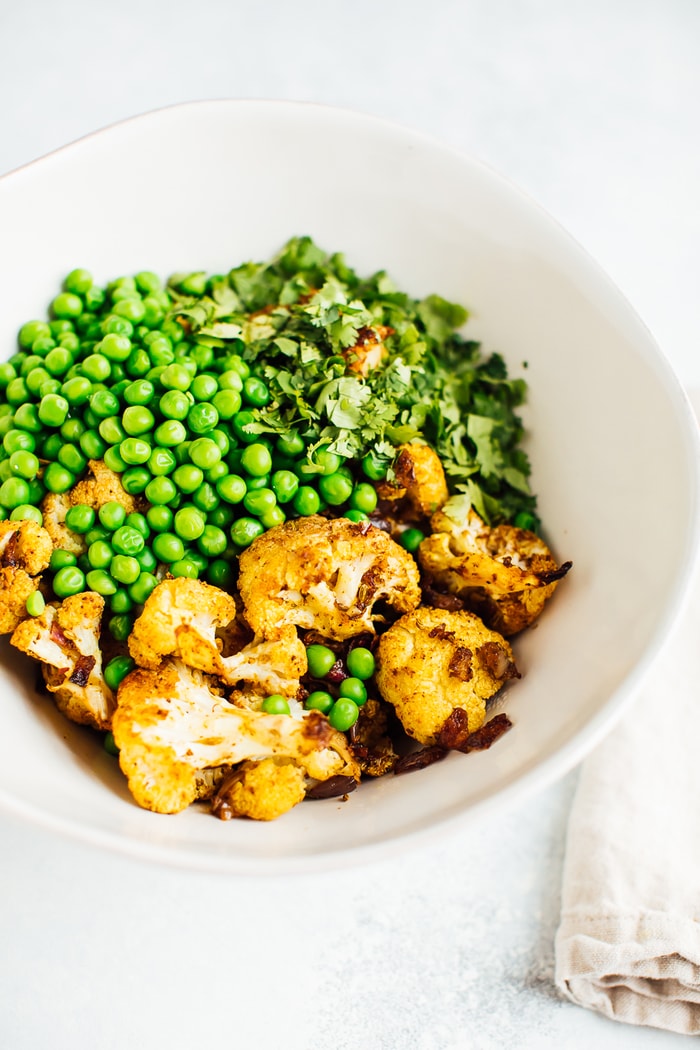 Curry roasted cauliflower, green peas and cilantro in a large white bowl. Curry roasted cauliflower, green peas and cilantro in a large white bowl.