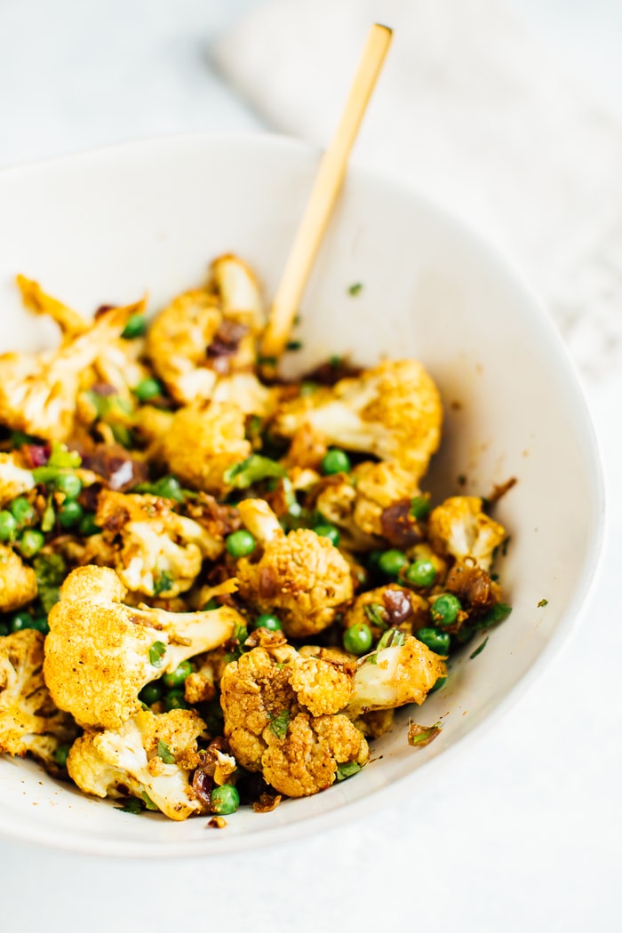 Mixing the roasted curried cauliflower with the green peas and cilantro using a gold spoon.