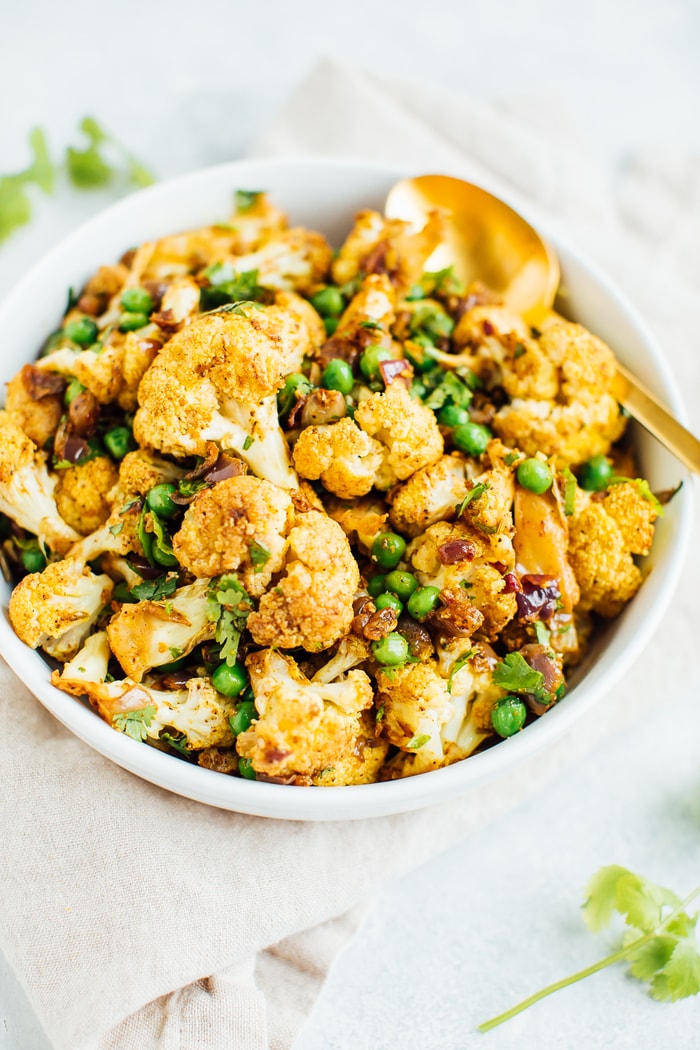 Pin this recipe --> CRACKLING CAULIFLOWER! A curried cauliflower salad with green peas and cilantro in a large white bowl with a gold spoon.
