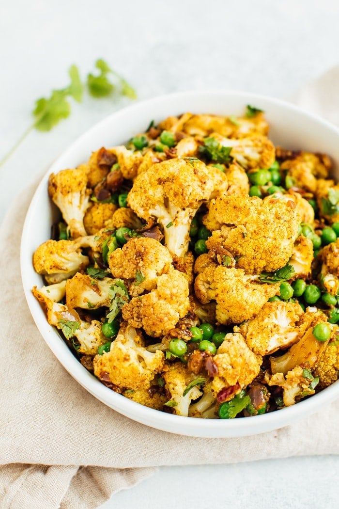 Pin this recipe --> CURRIED CAULIFLOWER SALAD A curried cauliflower salad with green peas and cilantro in a large white bowl with a gold spoon.