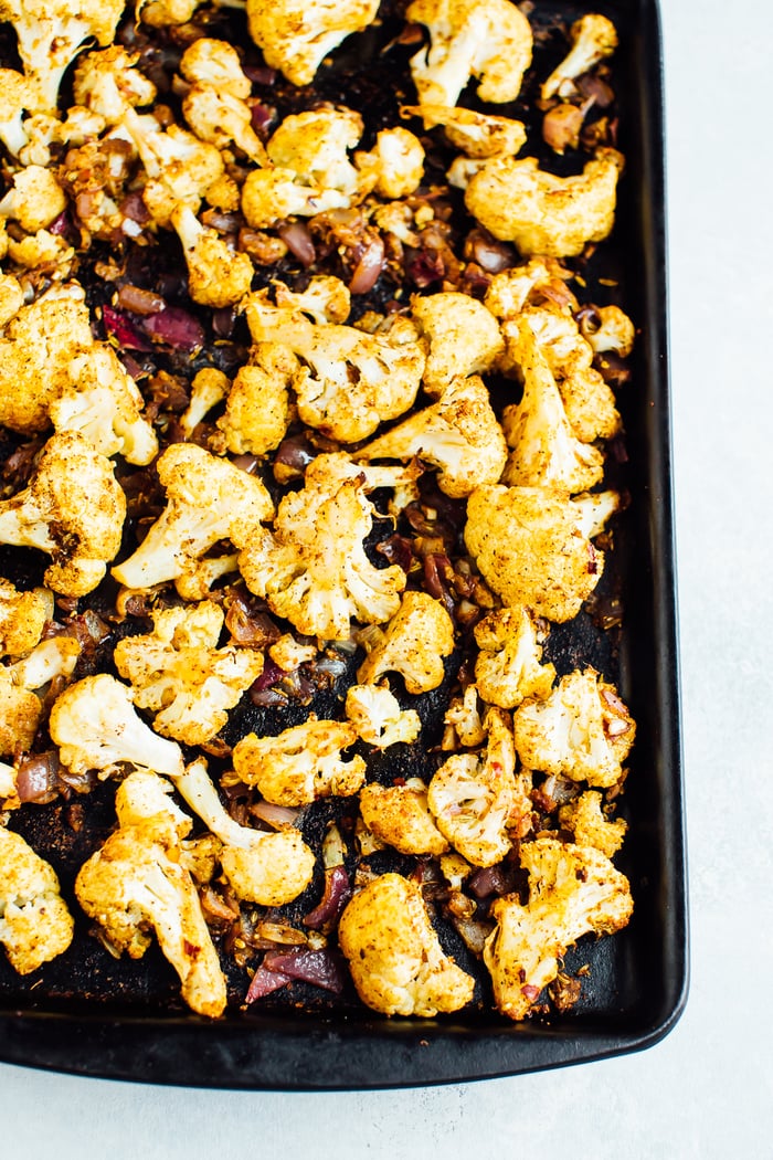 Roasted cauliflower and red onion on a stone baking sheet.
