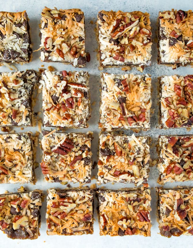 Multiple magic cookie bars in a row near one another on parchment paper.