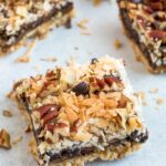 A cookie bar with almond flour cookie crust topped with coconut caramel, coconut, pecans, and chocolate chips.