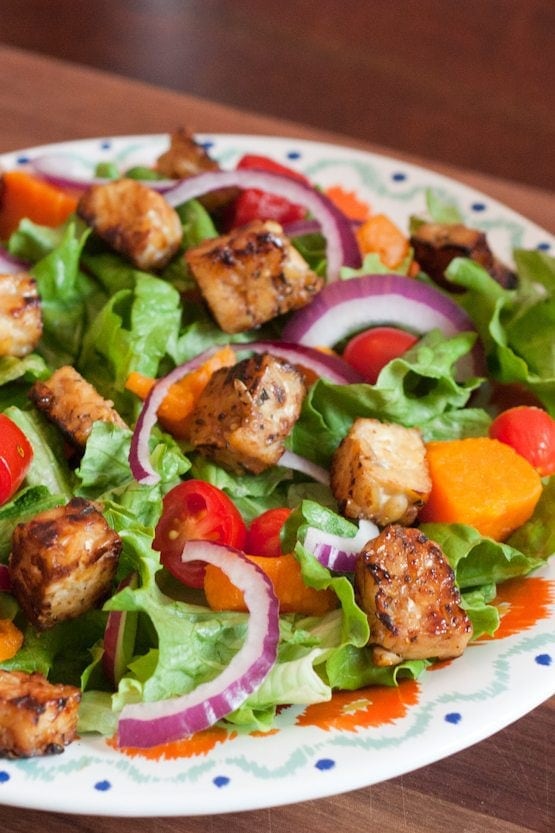 Maple Lemon Tempeh Cubes -- Great for Topping Salads or Snacking A bed of salad greens with red onion slices and maple lemon tempeh cubes on a dinner plate.