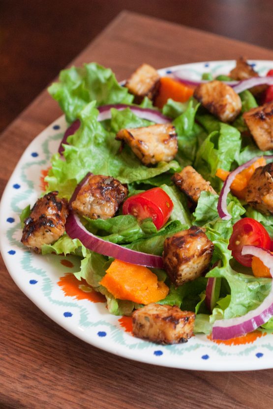 Maple Lemon Tempeh Cubes -- Great for Topping Salads or Snacking A bed of salad greens with red onion slices and maple lemon tempeh cubes on a dinner plate.