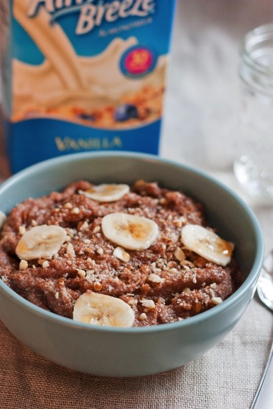 Banana Almond Teff Porridge served in a light blue bowl with an almond milk container in background.