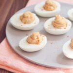 Hummus deviled eggs served on a white plate with a pink napkin underneath.