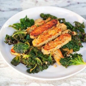 Lemon garlic tempeh slices over a bed of cooked kale served on a white plate.