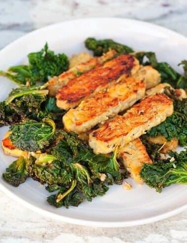 Lemon garlic tempeh slices over a bed of cooked kale served on a white plate.