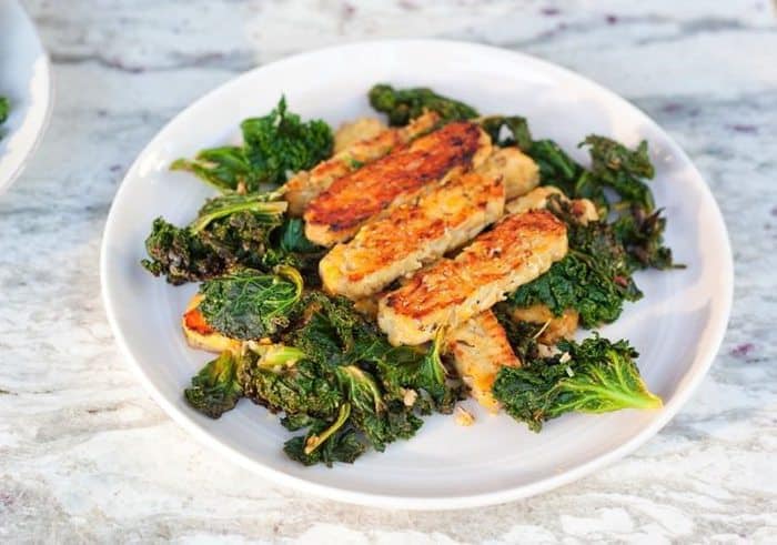 Lemon garlic tempeh slices over a bed of cooked kale served on a white plate.