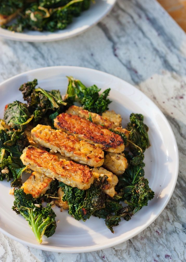 PIN THIS--> Lemon Garlic Tempeh Lemon garlic tempeh slices served over a bed of cooked kale on a white plate.