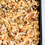 A large baking tray of freshly made coconut granola with toasted coconut and various nuts and seeds.