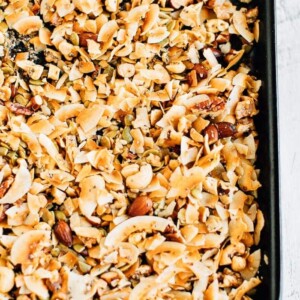 A large baking tray of freshly made coconut granola with toasted coconut and various nuts and seeds.