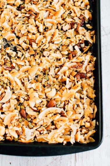 A large baking tray of freshly made coconut granola with toasted coconut and various nuts and seeds.