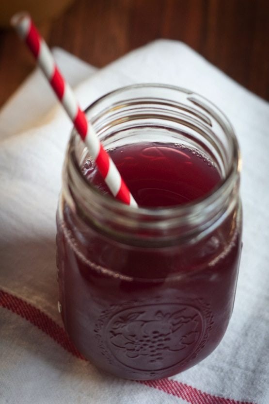 Save this Delicous Detox Drink recipe! Mason jar with purple liquid and red and white striped straw sitting on a white towel.
