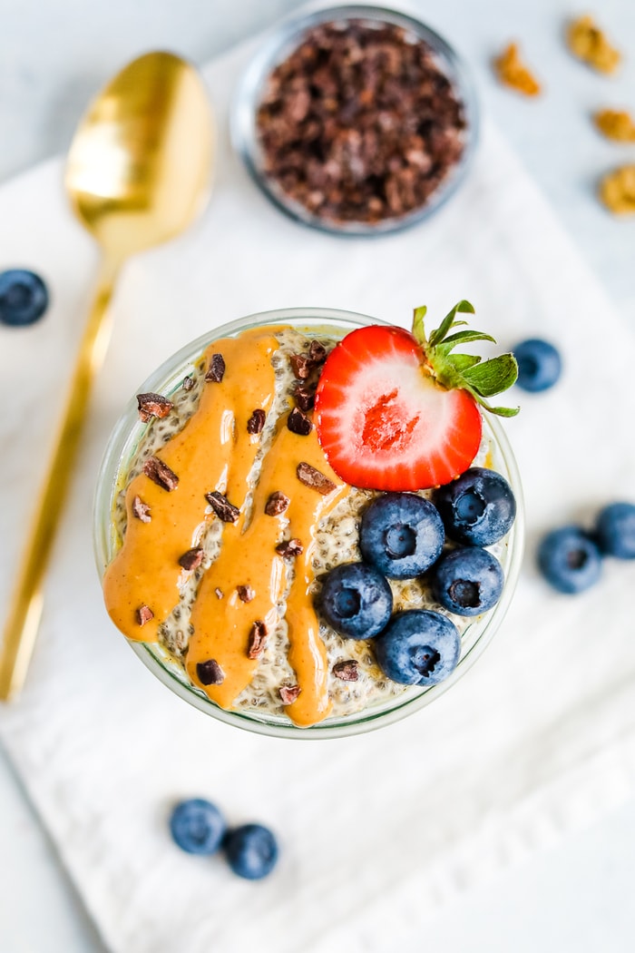 Jar of peanut butter chia seed pudding topped with cacao nibs, blueberries, and a strawberry.