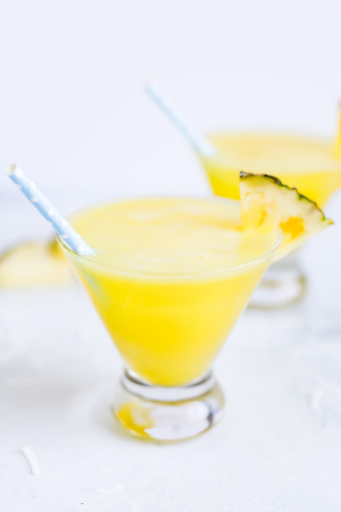 Two skinny piña coladas in glass cups with blue polka dot paper straws.