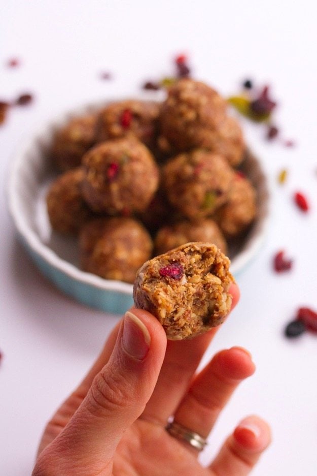 PIN THIS--> Superfood Energy Balls Hand holding Superfood Energy Ball with a bite out of it in the foreground, superfood berries and shallow bowl of superfood energy balls in the background.