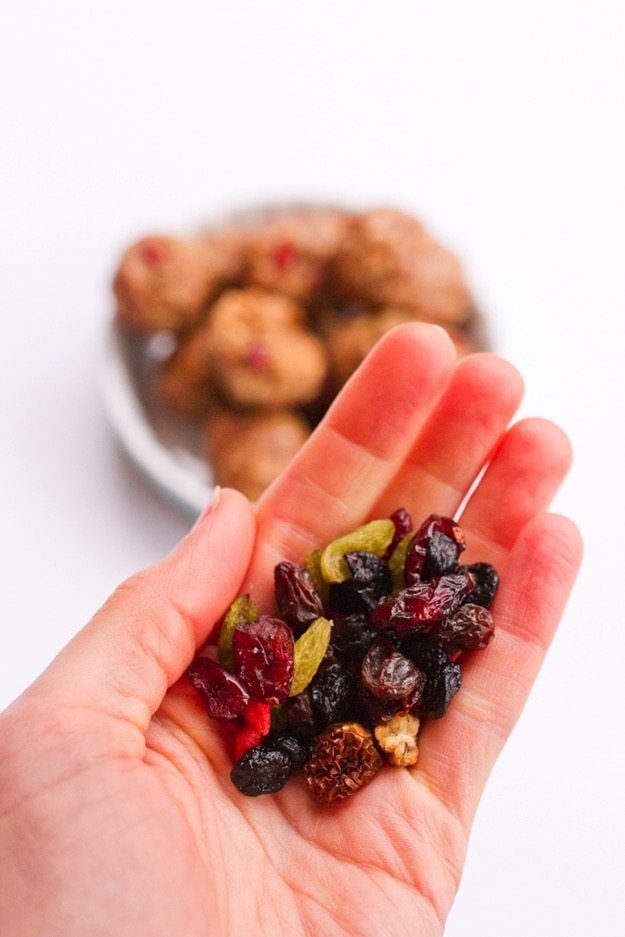 PIN THIS--> Superfood Energy Balls Superfood berries in the palm of a hand with superfood energy balls in the background.